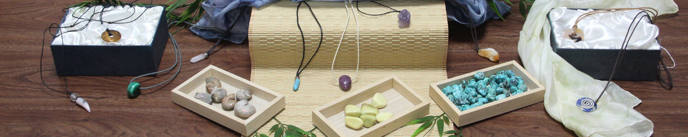 Das Bild zeigt diverse Edelsteine als Ketten und Trommelsteine in verschiedenen Boxen und auf dem Boden. Als Deko liegen bunte Tücher dazwischen.