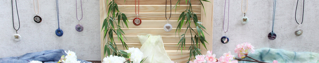 Das Bild zeigt diverse Edelstein Donuts als Ketten an einer weißen Wand. Als Deko liegen bunte Tücher und Kirschblüten auf dem Boden.