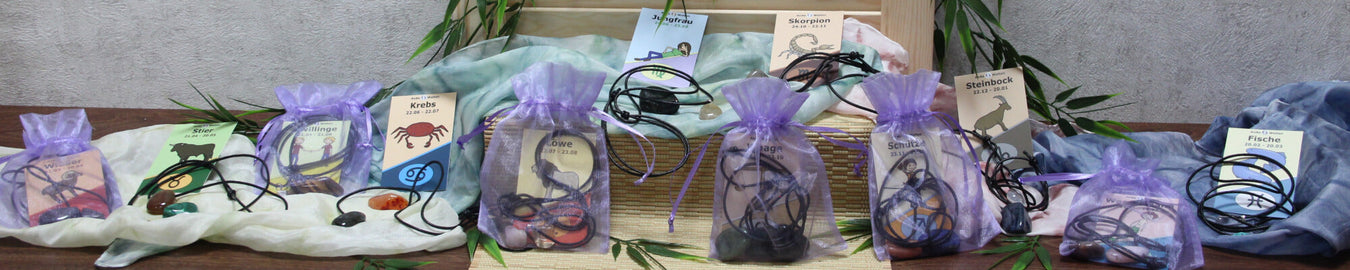 Das Bild zeigt 12 Sternzeichen Sets. Als Deko liegen bunte Tücher und Bambus dazwischen.
