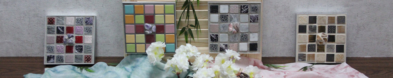 Das Bild zeigt 4 Sator Quadrat Mosaike vor einer weißen Wand. Als Deko liegen bunte Tücher, Bambus und Blumen dazwischen.