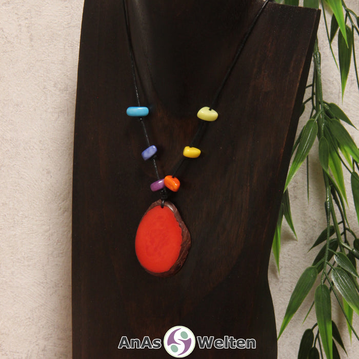 Eine rote Tagua-Nuss Scheibe als Chakra Kette mit 6 Tagua-Splittern in den anderen Chakrafarben an einer dunklen Büste.