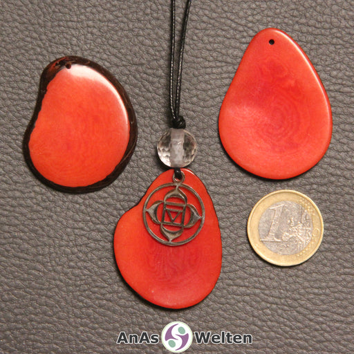 Drei rot gefärbte Tagua-Nuss-Scheiben. Eine davon ist als Kette mit Bergkristall und 1. Chakra Symbol gebunden.