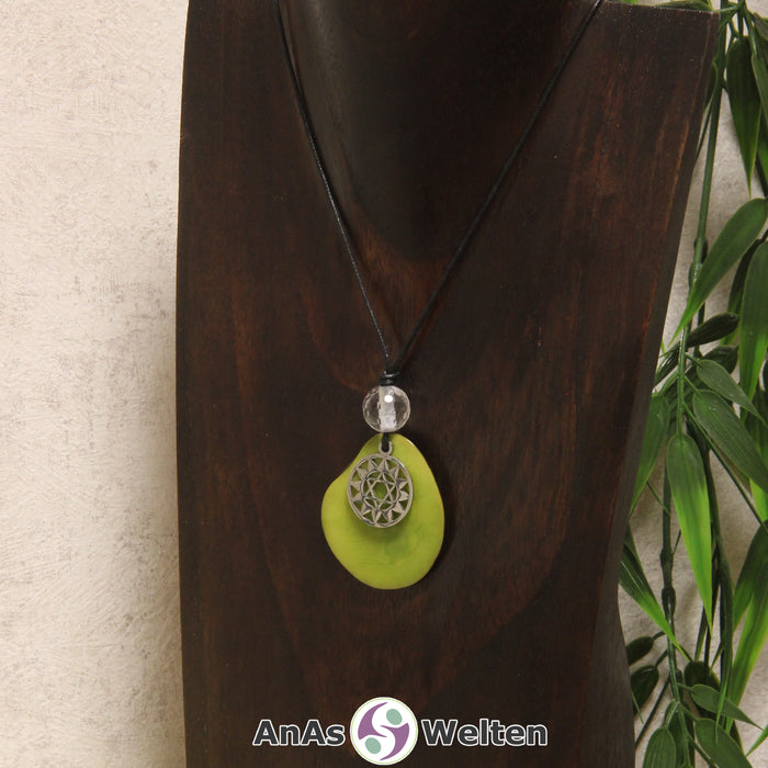 Eine grüne Tagua-Nuss Chakra Kette mit silberfarbenem 4. Chakra Symbol und Bergkristallkugel an einer dunklen Büste.