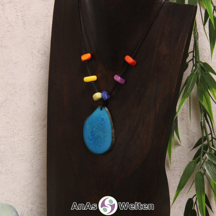 Eine türkise Tagua-Nuss Scheibe als Chakra Kette mit 6 Tagua-Splittern in den anderen Chakrafarben an einer dunklen Büste.