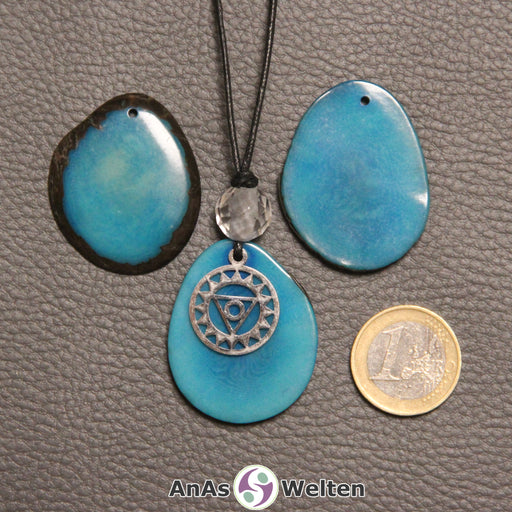 Drei türkis gefärbte Tagua-Nuss-Scheiben. Eine davon ist als Kette mit Bergkristall und 5. Chakra Symbol gebunden.
