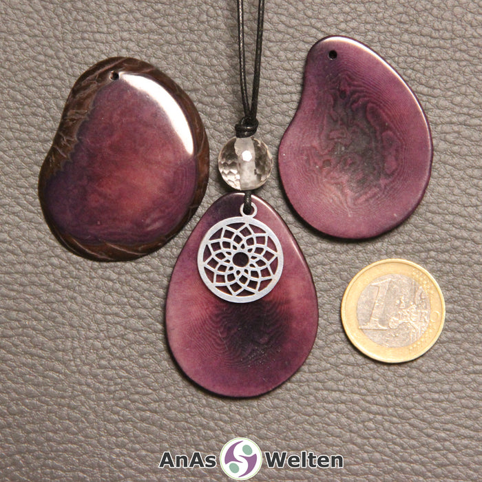 Drei lila gefärbte Tagua-Nuss-Scheiben. Eine davon ist als Kette mit Bergkristall und 7. Chakra Symbol gebunden.