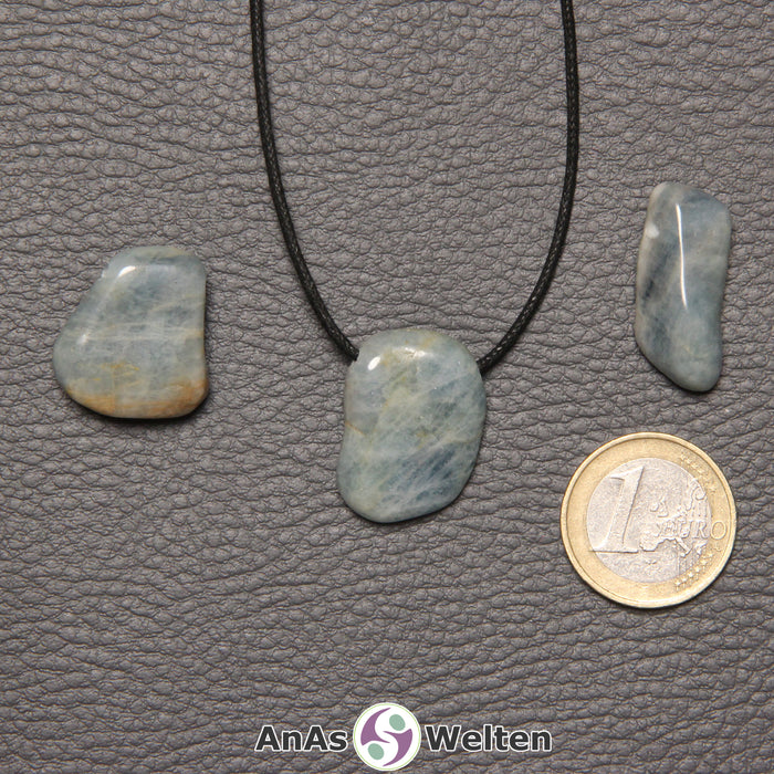 Drei blaue Aquamarin gebohrte Trommelsteine nebeneinander. Einer befindet sich an einem schwarzen gewachsten Baumwollband.