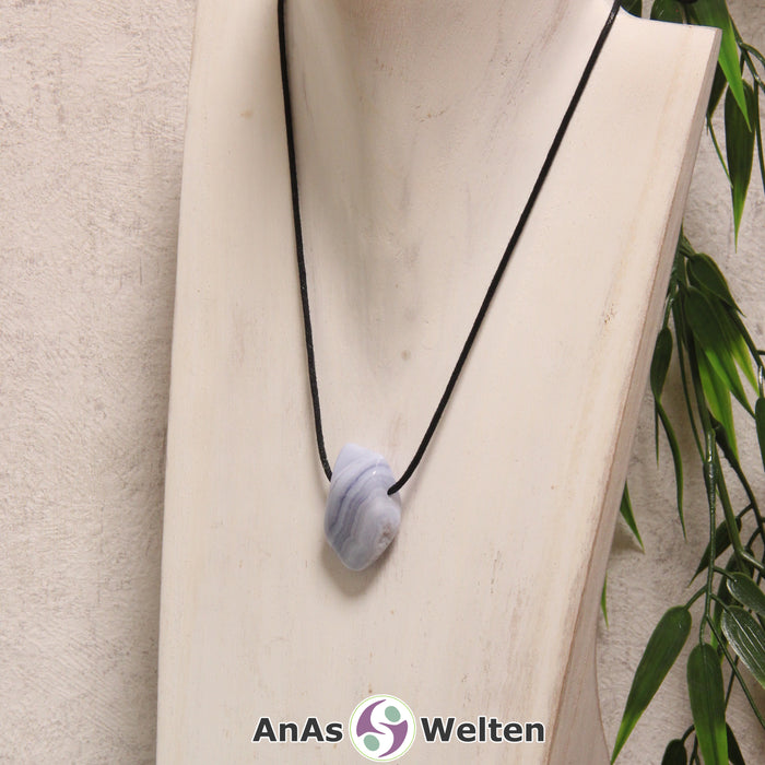 Ein blauer Chalcedon gebohrter Trommelstein an einem schwarzen Baumwollband, der um eine helle Büste gehängt wurde.