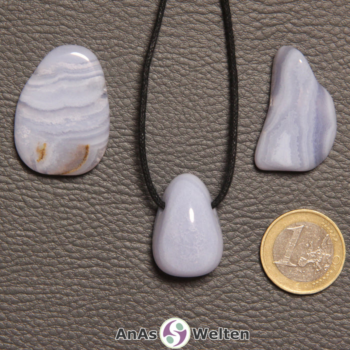Drei blauer Chalcedon gebohrte Trommelsteine nebeneinander. Einer befindet sich an einem schwarzen gewachsten Baumwollband.