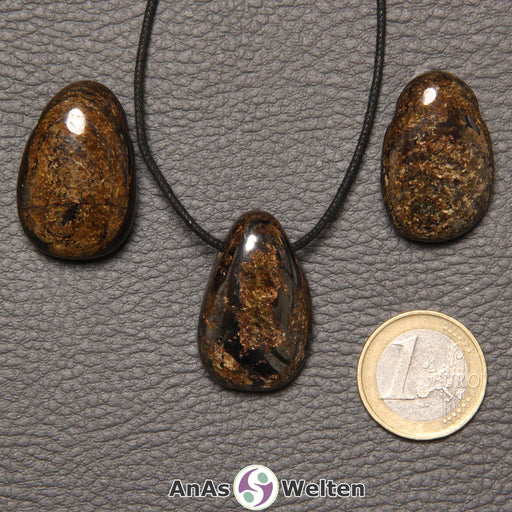 Drei braune Bronzit gebohrte Trommelsteine nebeneinander. Einer befindet sich an einem schwarzen gewachsten Baumwollband.