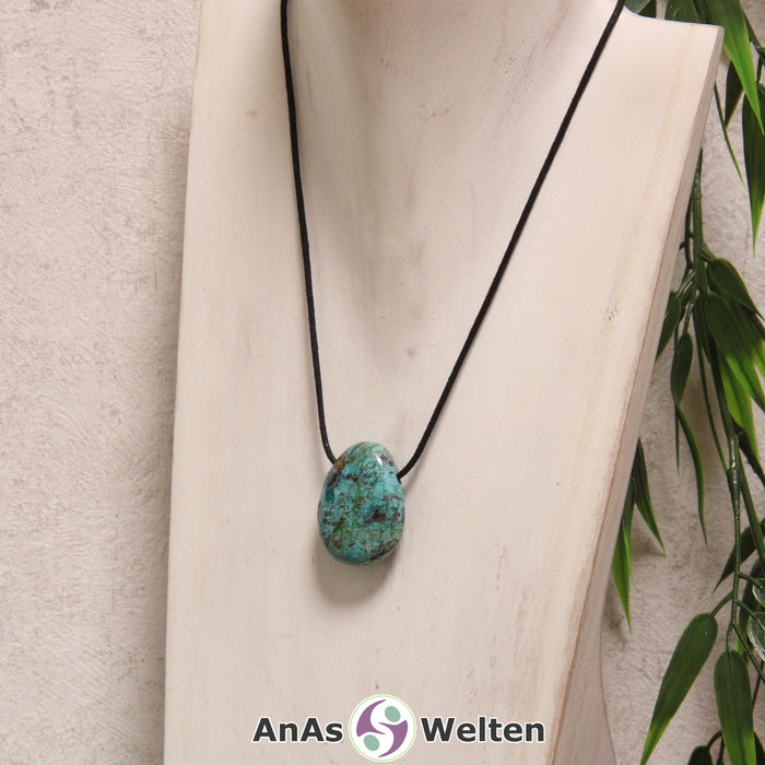 Ein blau-grüner Chrysokoll gebohrter Trommelstein an einem schwarzen Baumwollband, der um eine helle Büste gehängt wurde.