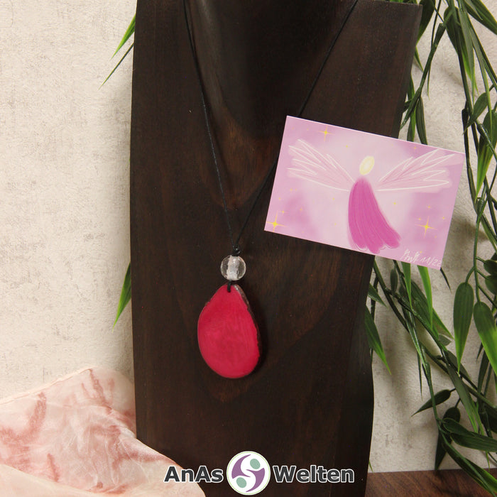 Ein pinker Tagua-Nuss Engel Anhänger ist als Kette mit einer Bergkristallkugel um eine dunkle Büste gehängt.