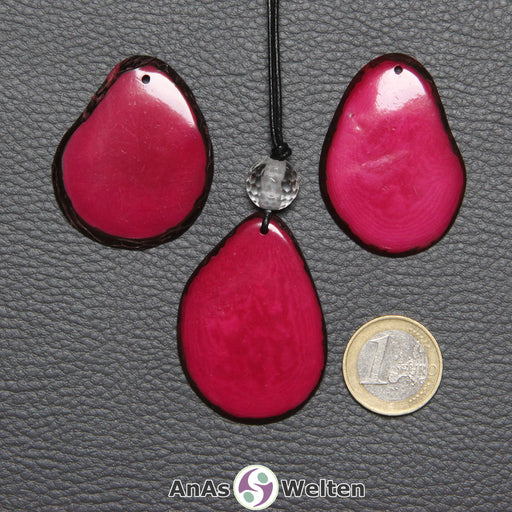Drei Tagua-Nuss-Scheiben in Pink. Die mittlere ist mit einer Bergkristallkugel an ein schwarzes Baumwollband gebunden.
