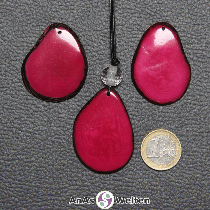 Drei Tagua-Nuss-Scheiben in Pink. Die mittlere ist mit einer Bergkristallkugel an ein schwarzes Baumwollband gebunden.