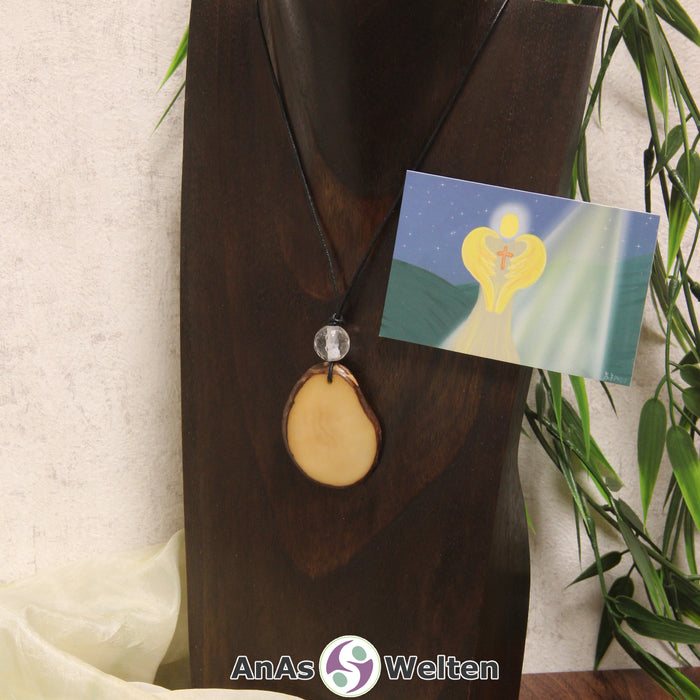 Ein gelber Tagua-Nuss Engel Anhänger ist als Kette mit einer Bergkristallkugel um eine dunkle Büste gehängt.