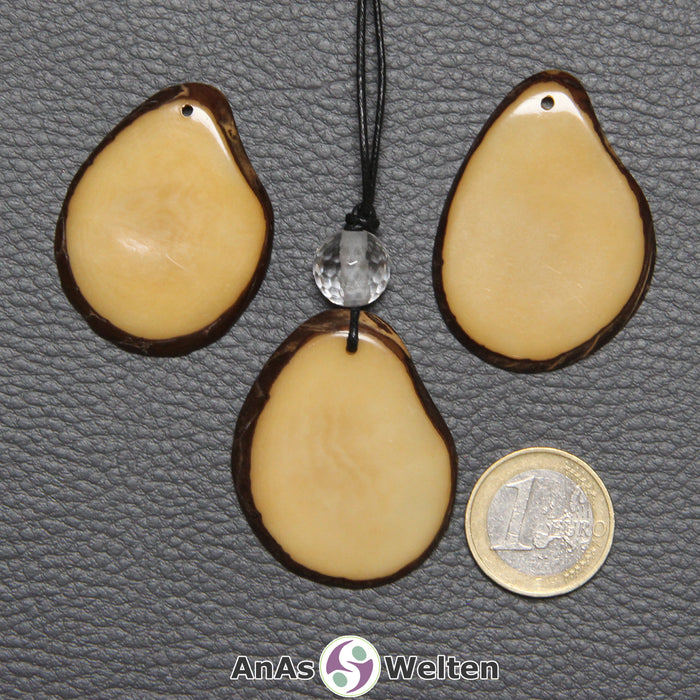 Drei Tagua-Nuss-Scheiben in Gelb. Die mittlere ist mit einer Bergkristallkugel an ein schwarzes Baumwollband gebunden.