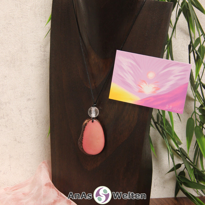 Ein rosa Tagua-Nuss Engel Anhänger ist als Kette mit einer Bergkristallkugel um eine dunkle Büste gehängt.
