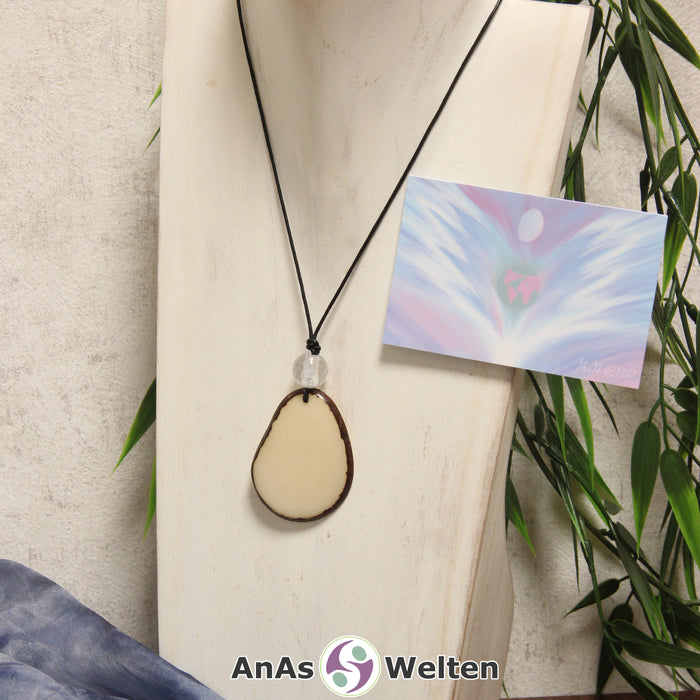 Ein Tagua-Nuss Engel Anhänger ist als Kette mit einer Bergkristallkugel um eine dunkle Büste gehängt.