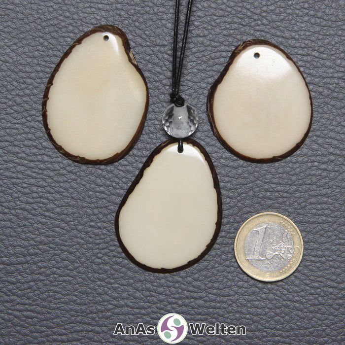 Drei Tagua-Nuss-Scheiben in Naturfarbe. Die mittlere ist mit einer Bergkristallkugel an ein schwarzes Baumwollband gebunden.