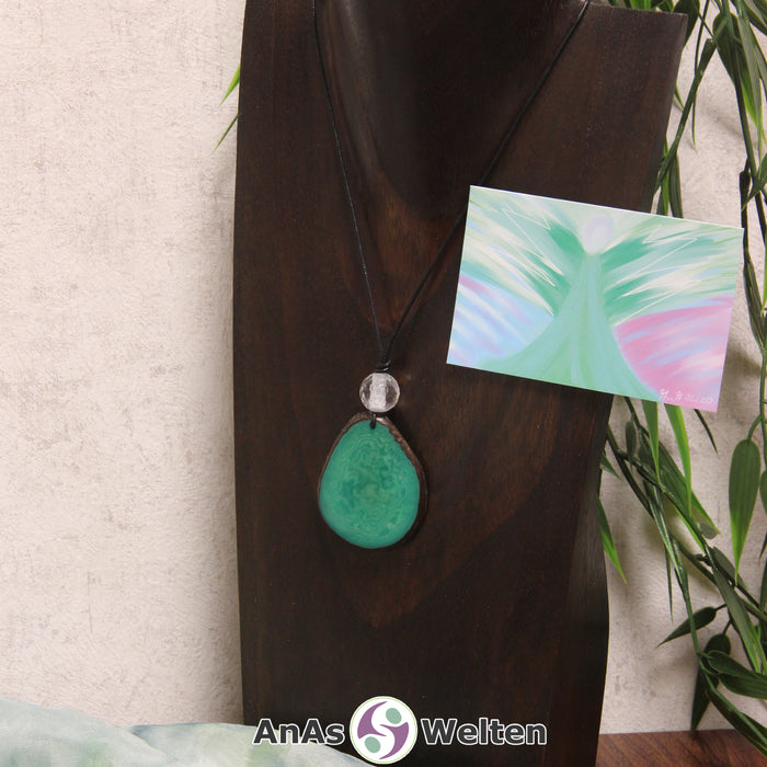 Ein grüner Tagua-Nuss Engel Anhänger ist als Kette mit einer Bergkristallkugel um eine dunkle Büste gehängt.