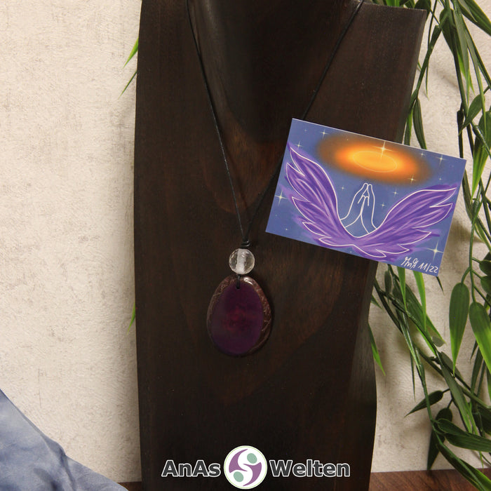 Ein lila Tagua-Nuss Engel Anhänger ist als Kette mit einer Bergkristallkugel um eine dunkle Büste gehängt.