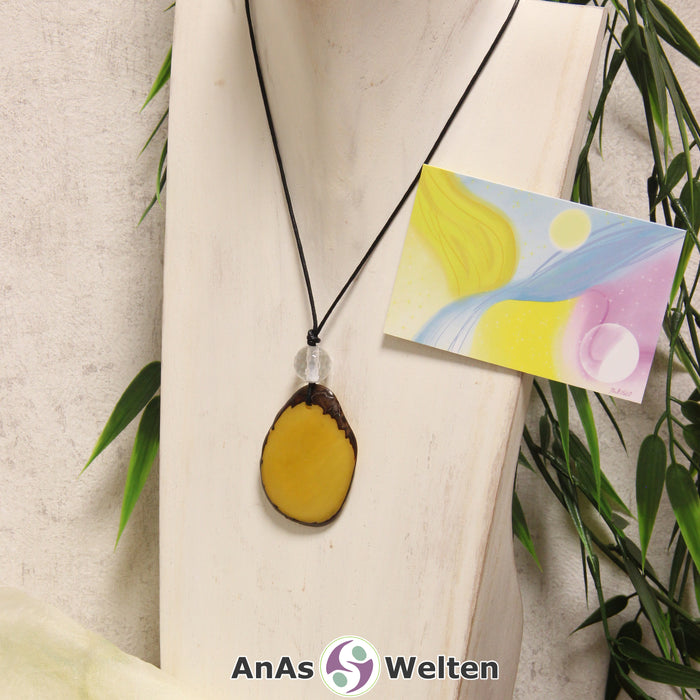 Ein gelber Tagua-Nuss Engel Anhänger ist als Kette mit einer Bergkristallkugel um eine dunkle Büste gehängt.