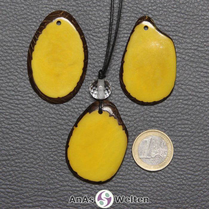 Drei Tagua-Nuss-Scheiben in Gelb. Die mittlere ist mit einer Bergkristallkugel an ein schwarzes Baumwollband gebunden.