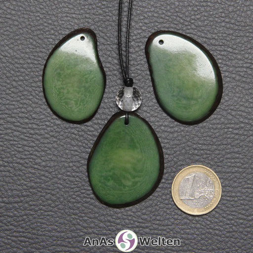 Drei Tagua-Nuss-Scheiben in Grün. Die mittlere ist mit einer Bergkristallkugel an ein schwarzes Baumwollband gebunden.