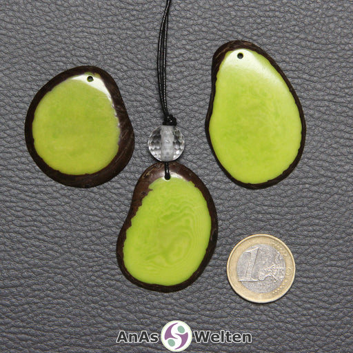 Drei Tagua-Nuss-Scheiben in Grün. Die mittlere ist mit einer Bergkristallkugel an ein schwarzes Baumwollband gebunden.