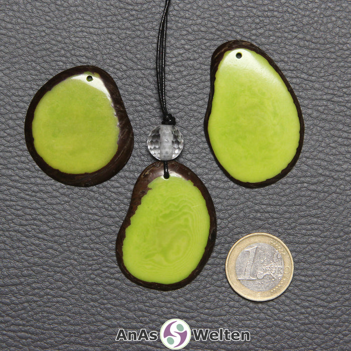 Drei Tagua-Nuss-Scheiben in Grün. Die mittlere ist mit einer Bergkristallkugel an ein schwarzes Baumwollband gebunden.
