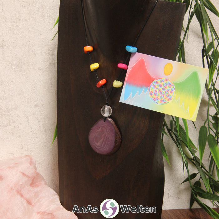 Ein lila Tagua-Nuss Engel Anhänger ist als Kette mit 6 bunten Tagua-Splittern und Bergkristallkugel um eine dunkle Büste gehängt.