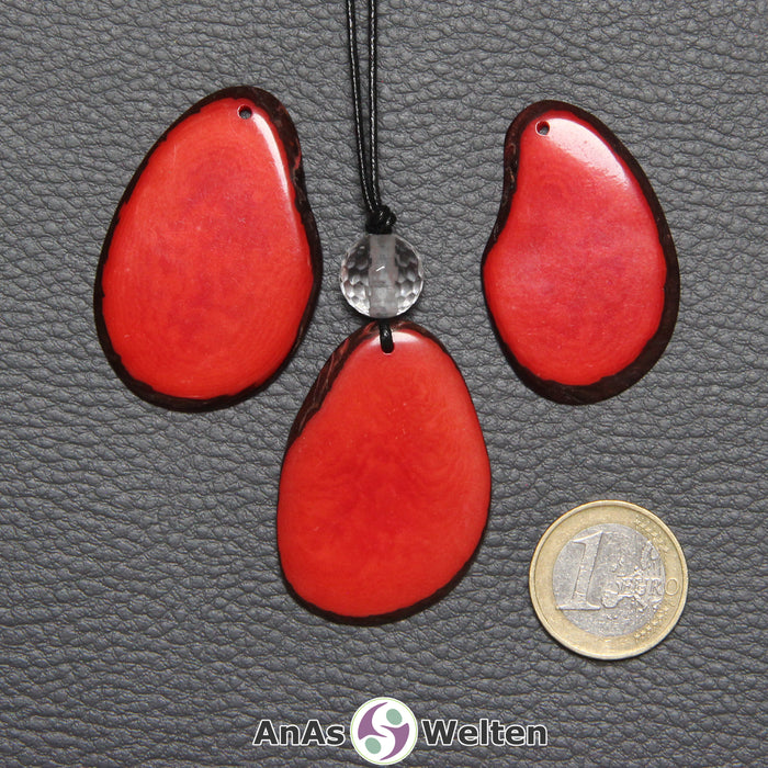 Drei Tagua-Nuss-Scheiben in Rot. Die mittlere ist mit einer Bergkristallkugel an ein schwarzes Baumwollband gebunden.