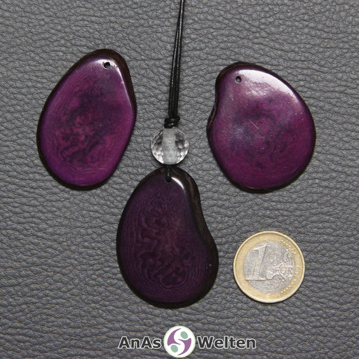 Drei Tagua-Nuss-Scheiben in Lila. Die mittlere ist mit einer Bergkristallkugel an ein schwarzes Baumwollband gebunden.