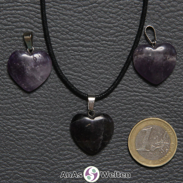 Drei Herzanhänger aus Amethyst nebeneinander. Einer befindet sich an einem schwarzen gewachsten Baumwollband.