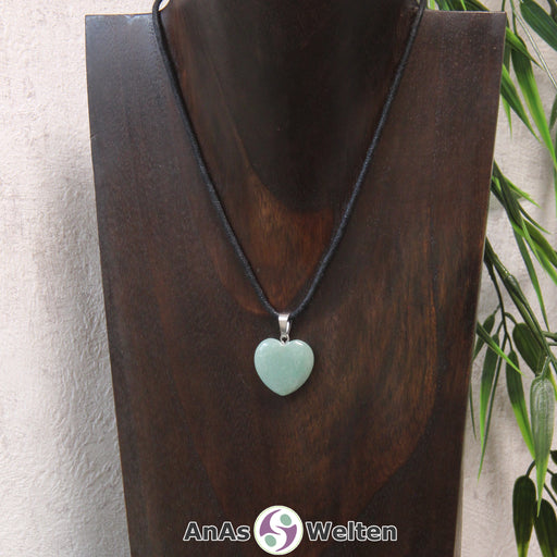 Das Bild zeigt einen Herzanhänger Aventurin-Herz an einem schwarzen Baumwollband. Der Edelstein wurde in eine Herzform geschliffen und verfügt über eine silberfarbene Öse an der Oberseite. Er hat eine gleichmäßige hellblaue Farbe und ist ganz leicht durchsichtig, sodass man feine Risse unter seiner Oberfläche erkennen kann.