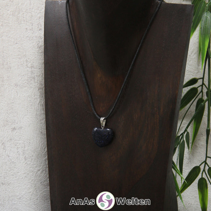 Ein Blaufluss Herz Anhänger an einem schwarzen Baumwollband, der um eine dunkle Büste gehängt wurde.