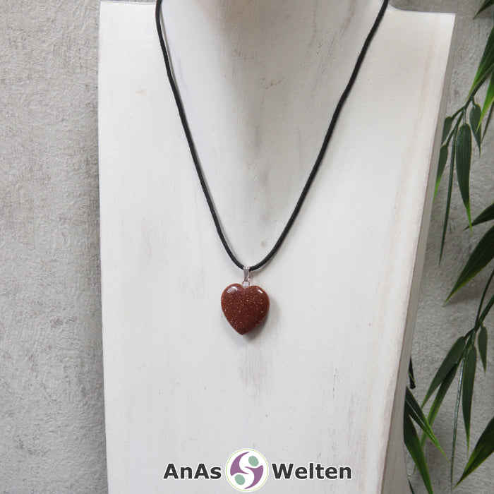 Ein Goldfluss Herz Anhänger an einem schwarzen Baumwollband, der um eine helle Büste gehängt wurde.