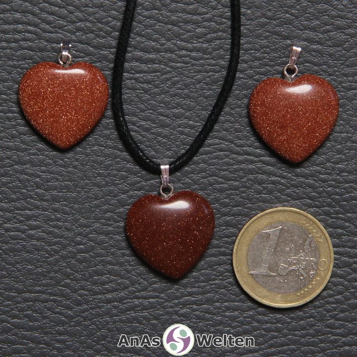 Drei Herzanhänger aus Goldfluss nebeneinander. Einer befindet sich an einem schwarzen gewachsten Baumwollband.