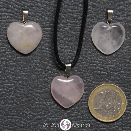Drei Herzanhänger aus Rosenquarz nebeneinander. Einer befindet sich an einem schwarzen gewachsten Baumwollband.