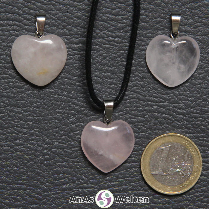 Drei Herzanhänger aus Rosenquarz nebeneinander. Einer befindet sich an einem schwarzen gewachsten Baumwollband.