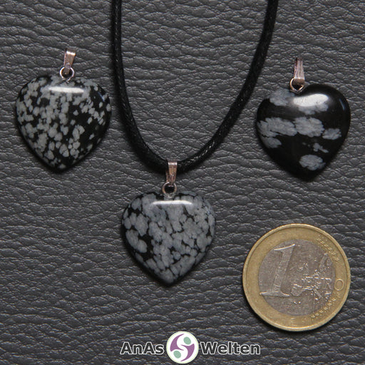 Drei Herzanhänger aus Schneeflocken-Obsidian nebeneinander. Einer befindet sich an einem schwarzen gewachsten Baumwollband.