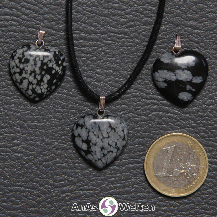 Drei Herzanhänger aus Schneeflocken-Obsidian nebeneinander. Einer befindet sich an einem schwarzen gewachsten Baumwollband.