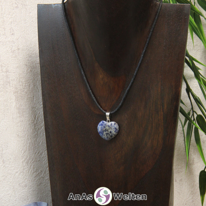 Ein Sodalith Herz Anhänger an einem schwarzen Baumwollband, der um eine dunkle Büste gehängt wurde.