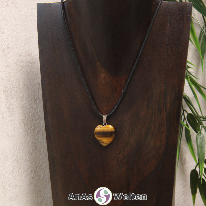 Ein Tigerauge Herz Anhänger an einem schwarzen Baumwollband, der um eine dunkle Büste gehängt wurde.