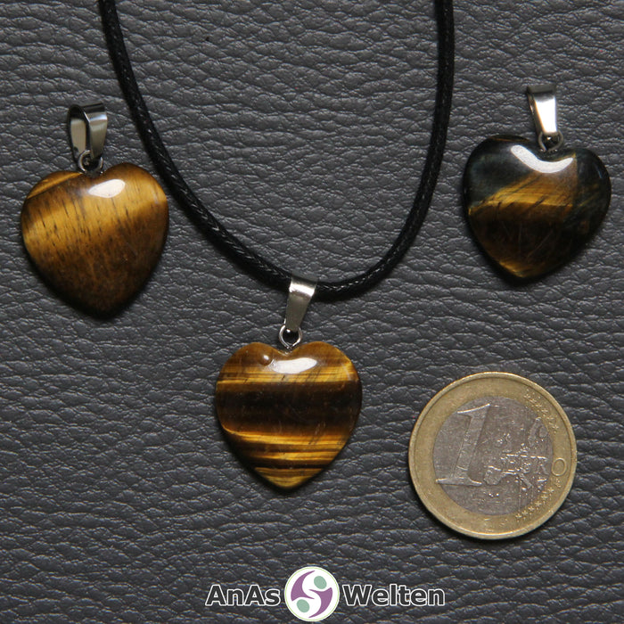 Drei Herzanhänger aus Tigerauge nebeneinander. Einer befindet sich an einem schwarzen gewachsten Baumwollband.