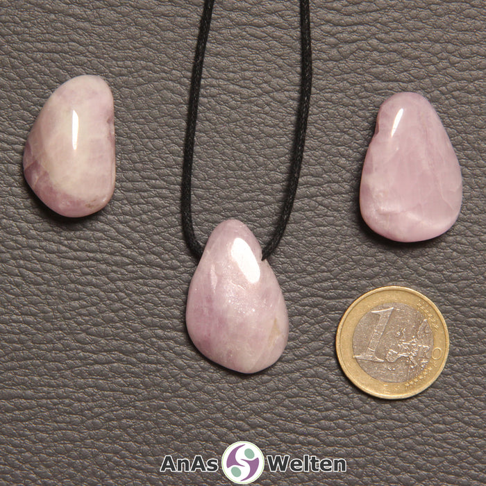 Drei rosa Kunzit gebohrte Trommelsteine nebeneinander. Einer befindet sich an einem schwarzen gewachsten Baumwollband.