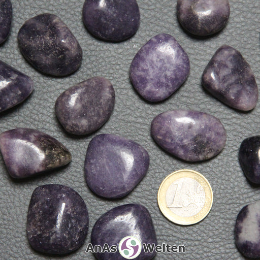 Das Bild zeigt einen Lepidolith Trommelstein anhand von mehreren Beispielsteinen. Die Edelsteine haben eine hell- bis dunkellila Farbe mit einem unregelmäßigen Muster.