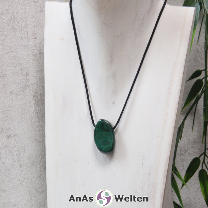 Ein grüner Malachit gebohrter Trommelstein an einem schwarzen Baumwollband, der um eine helle Büste gehängt wurde.