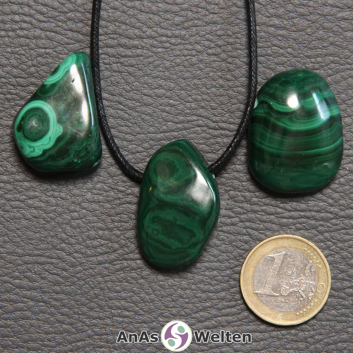 Drei grüne Malachit gebohrte Trommelsteine nebeneinander. Einer befindet sich an einem schwarzen gewachsten Baumwollband.
