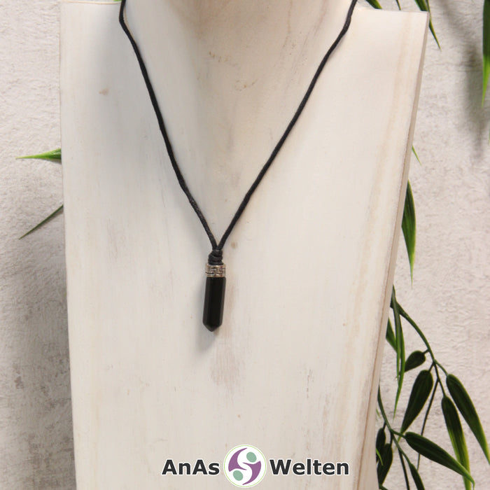 Das Bild zeigt einen Onyx Stift-Anhänger klein mit Kette. Der Stift-Anhänger ist tiefschwarz. Am oberen Ende verbindet ein silberfarbenes Element den Edelstein mit der Stoffkordel.